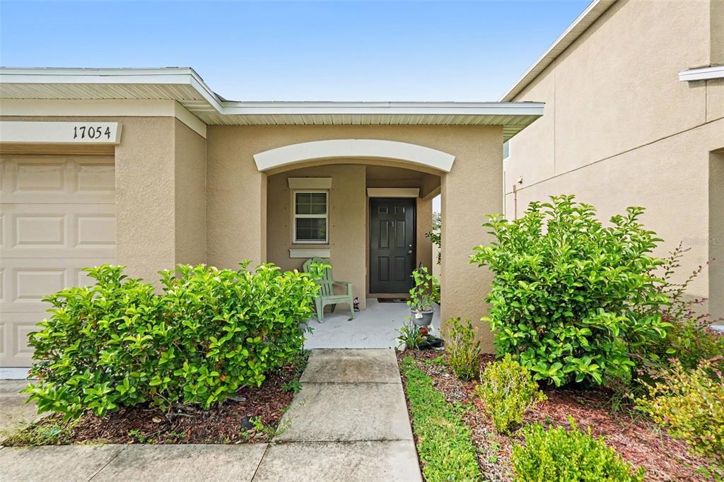 The exterior of a beige house features a front porch, a dark door, and landscaping — 17054 YELLOW PINE STREET, WIMAUMA, FL