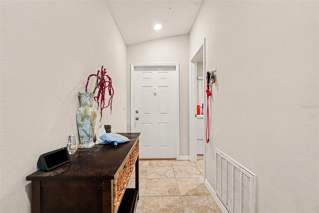 A tiled entryway features a dark wood console table, a white door, and beige walls — 17054 YELLOW PINE STREET, WIMAUMA, FL