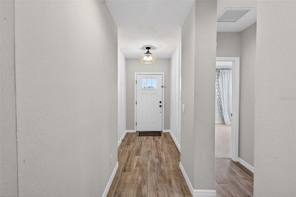 A hallway with light gray walls, wood-look flooring, and a white front door — 1245 CELERY OAKS LANE, SANFORD, FL