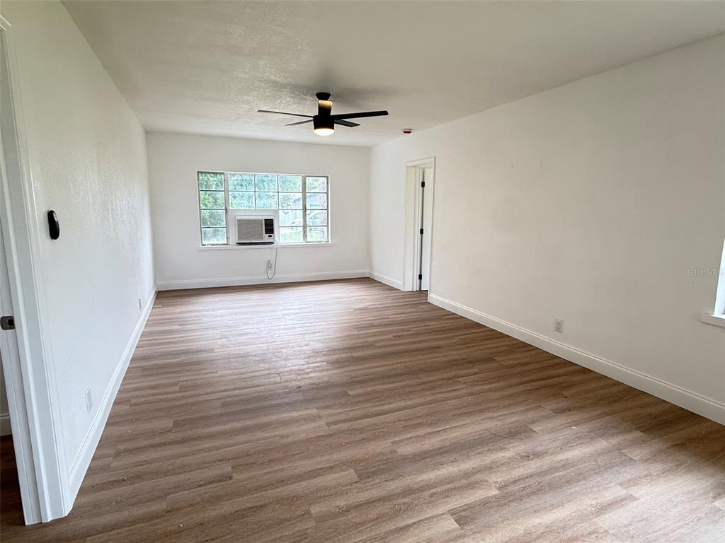 An empty room features light wood-look flooring, white walls, a ceiling fan, and a window unit — 165 E POMELO STREET, GROVELAND, FL