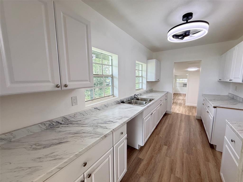 A kitchen features white cabinets, marble-look countertops, and wood-style flooring — 165 E POMELO STREET, GROVELAND, FL