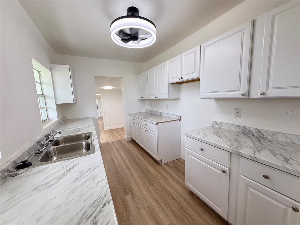 A kitchen features white cabinets, marble-patterned laminate countertops, and light wood-look flooring — 165 E POMELO STREET, GROVELAND, FL