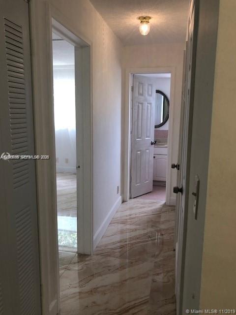 A hallway with light-colored marble-patterned tile flooring leads to a bathroom and another room — 1715 Wiley St # 5, Hollywood FL 33020, HOLLYWOOD, FL