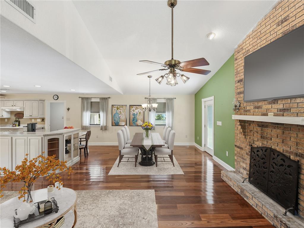 An open-concept dining room features a brick fireplace, hardwood floors, and a vaulted ceiling — 2955 GODWIN ROAD, ST CLOUD, FL