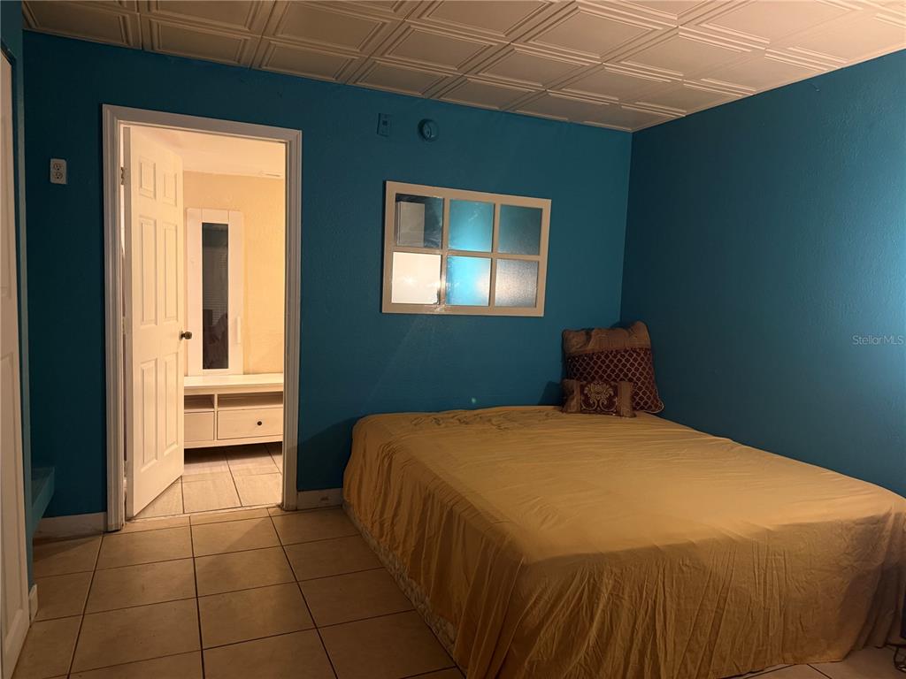 A bedroom with blue walls, a yellow bedspread, tile flooring, and a doorway to a bathroom — 8421 S ORANGE BLOSSOM TRAIL UNIT 339, ORLANDO, FL