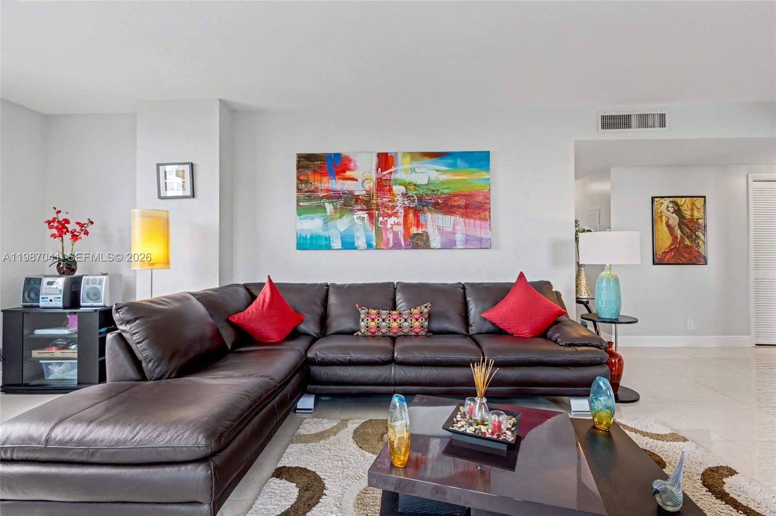 A living room features a dark leather sectional sofa, a colorful abstract painting, and tile flooring — 4330 Hillcrest Dr # 619, Hollywood FL 33021, HOLLYWOOD, FL