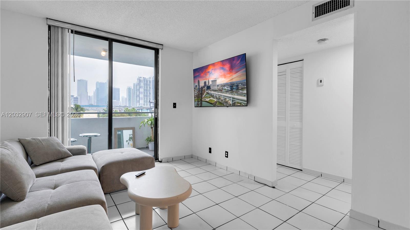 A living room features white tile floors, a grey sectional sofa, and a wall-mounted television — 546 SW 1st St # 603, Miami FL 33130, MIAMI, FL