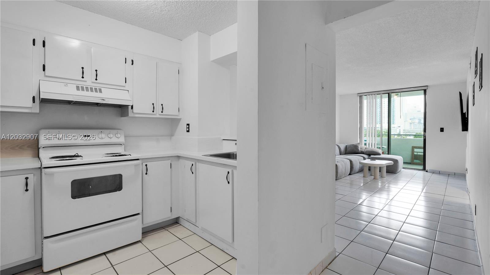 A white kitchen with tile flooring opens into a living area with a balcony view — 546 SW 1st St # 603, Miami FL 33130, MIAMI, FL