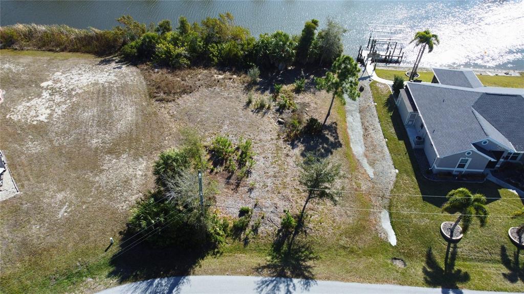 An aerial view shows a vacant waterfront lot with trees next to a residential house — 9548 ATTICA CIRCLE, PORT CHARLOTTE, FL