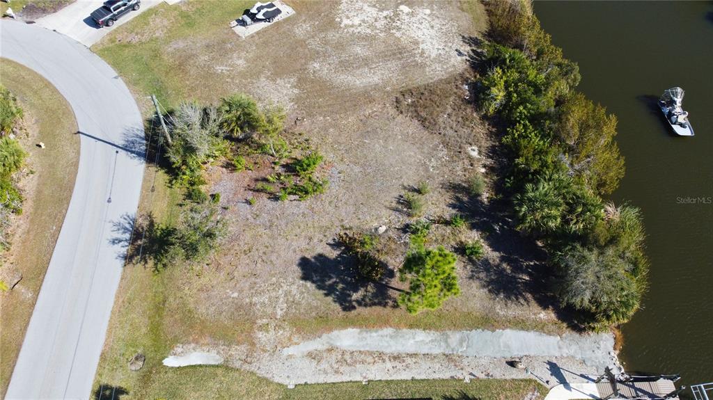 An aerial view shows a vacant waterfront lot with sparse vegetation and a boat dock — 9548 ATTICA CIRCLE, PORT CHARLOTTE, FL