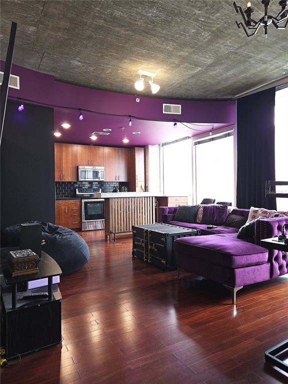 A modern living room and kitchen area features purple walls, a concrete ceiling, and wood floors — 155 S COURT AVENUE UNIT 1009, ORLANDO, FL