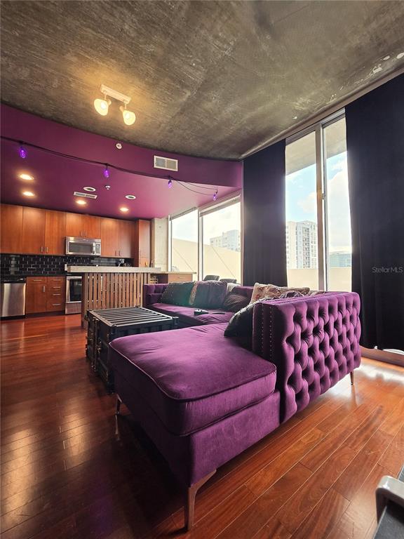 A living room features a purple velvet sectional, wood floors, and a concrete ceiling — 155 S COURT AVENUE UNIT 1009, ORLANDO, FL