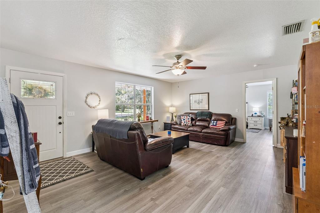 A living room features light-colored wood-look flooring, two brown leather sofas, and a ceiling fan — 5500 VENTURA ACRES ROAD, GROVELAND, FL