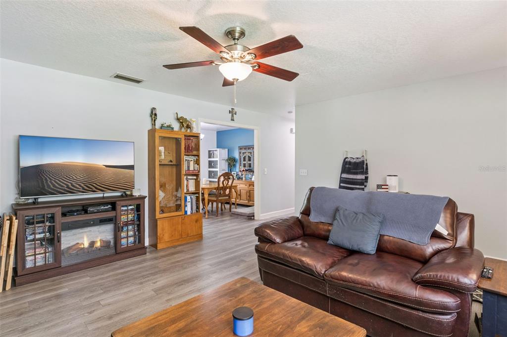 A living room features a leather sofa, a television on a fireplace console, and wood-look flooring — 5500 VENTURA ACRES ROAD, GROVELAND, FL