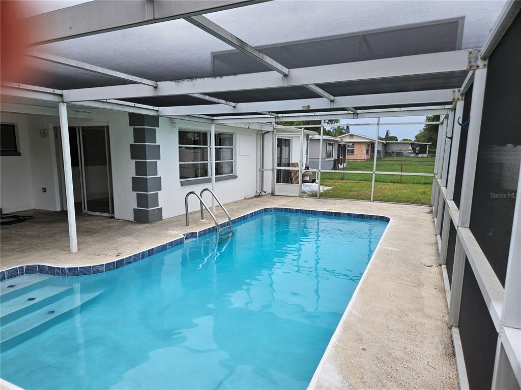 A screened-in backyard patio features a rectangular swimming pool with metal handrails — 6945 TWILITE DRIVE, PORT RICHEY, FL