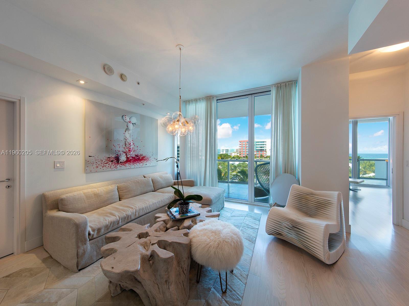 A modern living room features a beige sectional, sculptural wooden coffee tables, and floor-to-ceiling windows — 50 S Pointe Dr # 707, Miami Beach FL 33139, MIAMI BEACH, FL