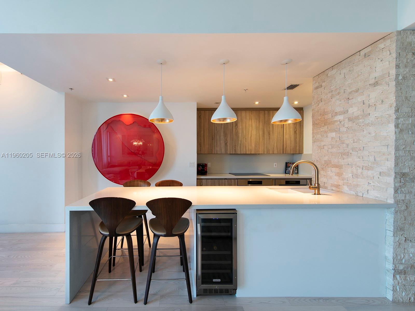 A modern kitchen features a white island with bar stools, a wine cooler, and pendant lighting — 50 S Pointe Dr # 707, Miami Beach FL 33139, MIAMI BEACH, FL