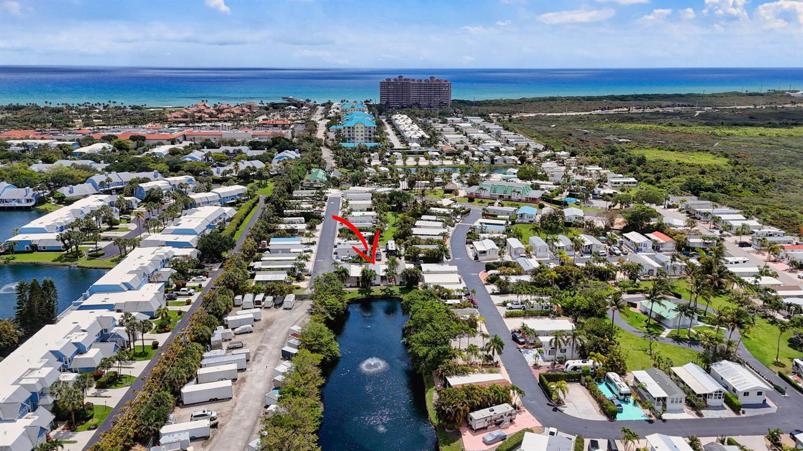 An aerial view shows a residential community with a central pond and a marked home — 900 Juno Ocean Walk # A71, Juno Beach FL 33408, JUNO BEACH, FL