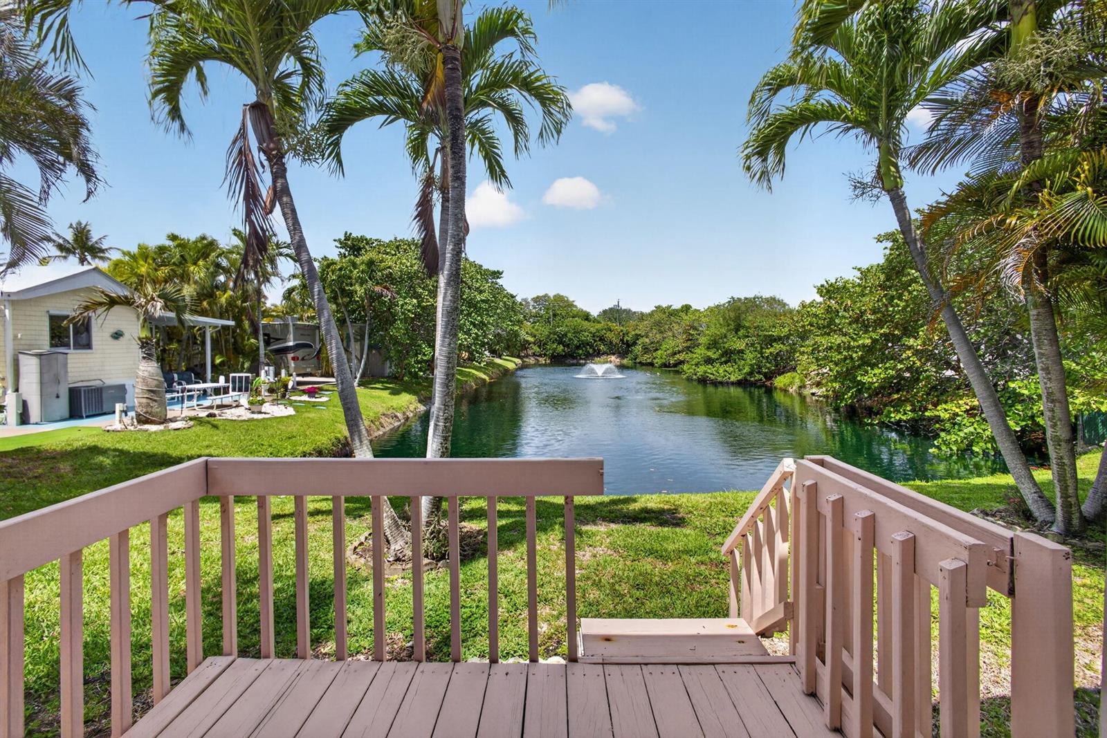 A wooden deck overlooks a pond with a fountain, surrounded by palm trees and grass — 900 Juno Ocean Walk # A71, Juno Beach FL 33408, JUNO BEACH, FL