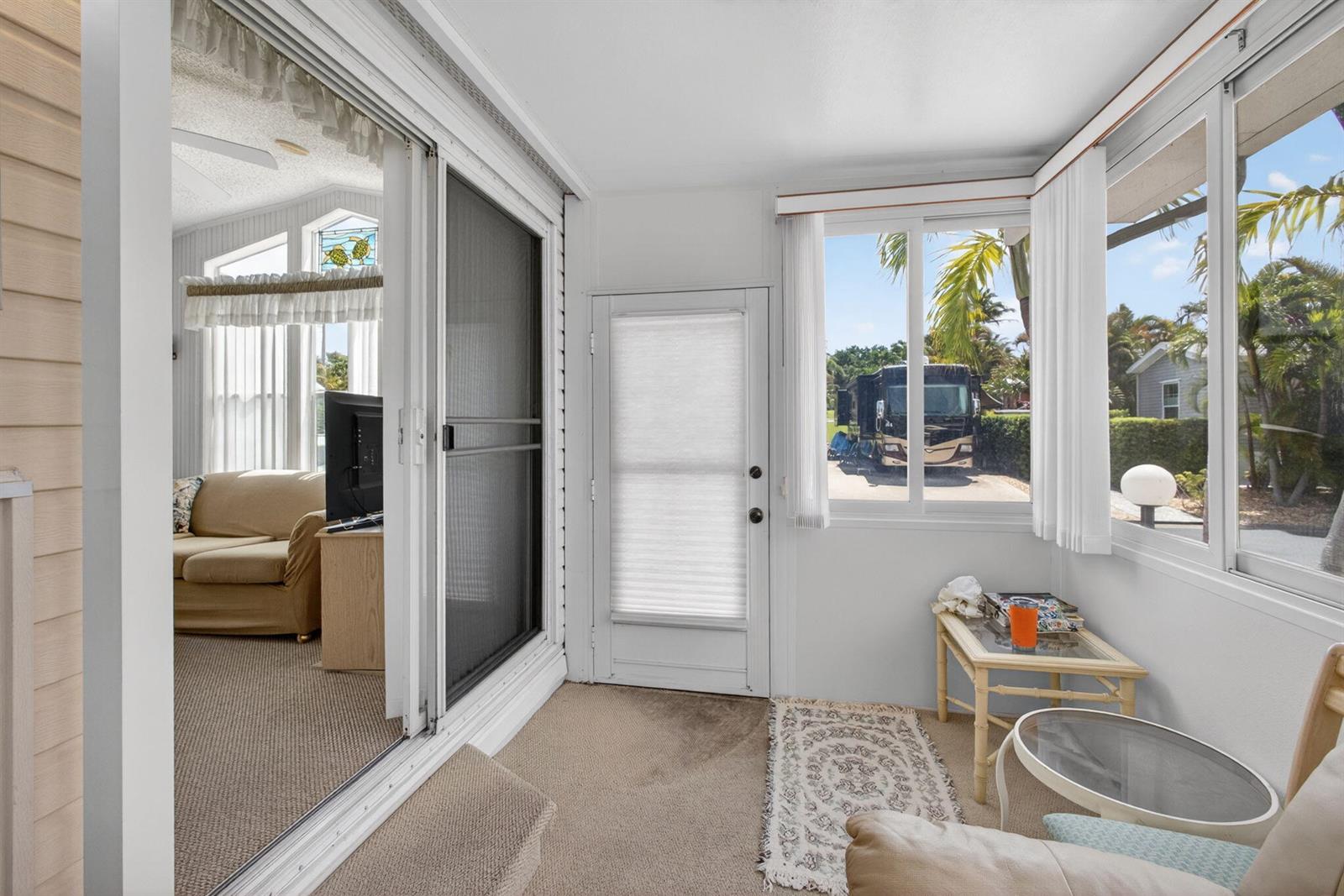 A sunroom with carpeted floors, a sliding glass door, and windows looking out at an RV — 900 Juno Ocean Walk # A71, Juno Beach FL 33408, JUNO BEACH, FL