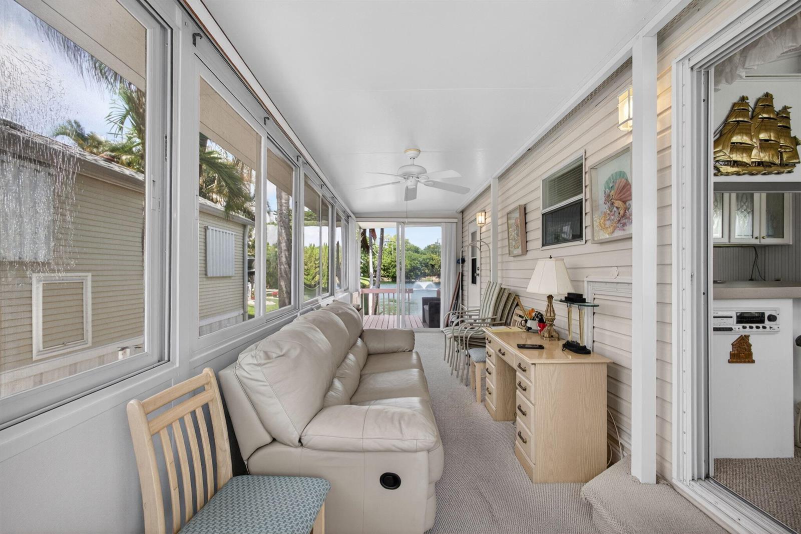 A sunroom features a light-colored sofa, a wooden desk, and large windows overlooking a pond — 900 Juno Ocean Walk # A71, Juno Beach FL 33408, JUNO BEACH, FL