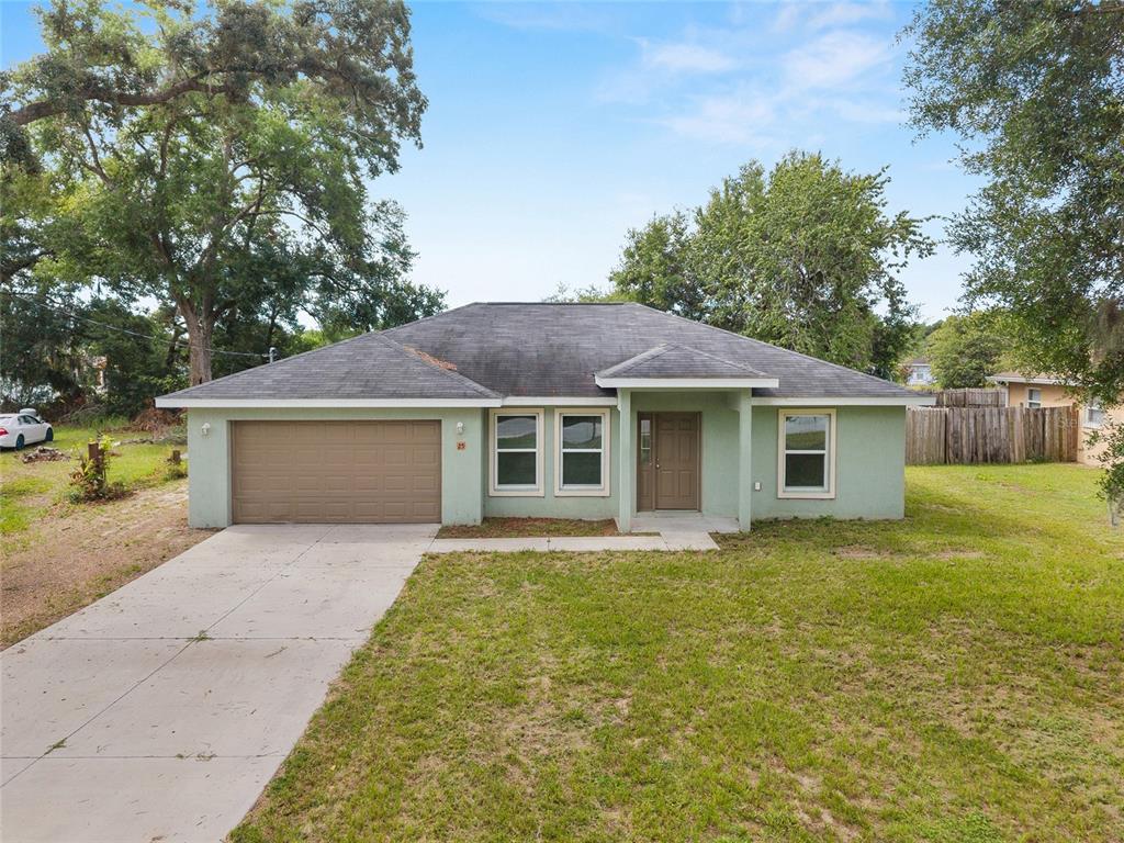 A single-story house with a light green exterior, a brown garage door, and a shingled roof — 25 DOGWOOD DRIVE TRAIL, OCALA, FL