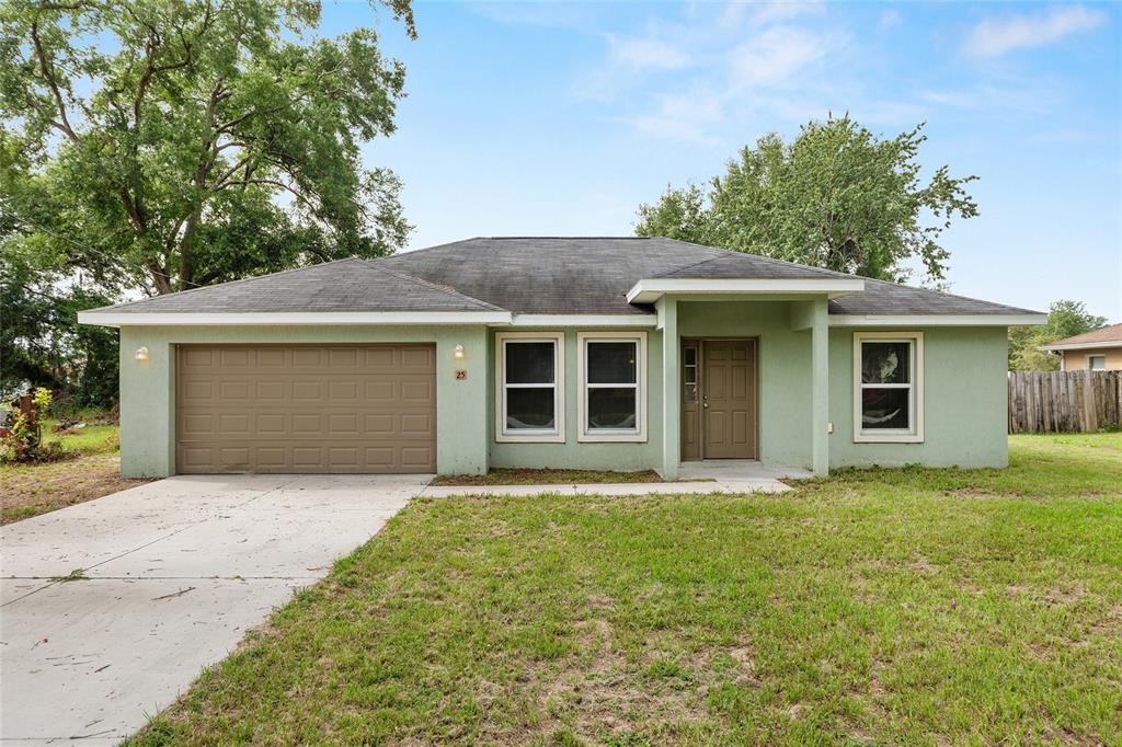 A single-story house with a green stucco exterior, a two-car garage, and a front porch — 25 DOGWOOD DRIVE TRAIL, OCALA, FL