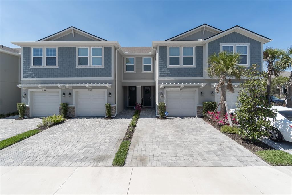 A two-story duplex with gray siding, white garage doors, and paved driveways under a blue sky — 8518 PRIMROSE WILLOW PLACE, ODESSA, FL