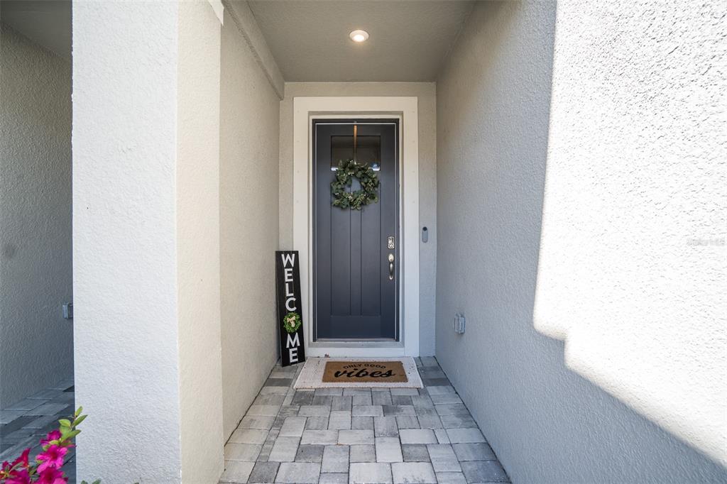 A gray front door with a wreath and welcome sign sits on a paved porch — 8518 PRIMROSE WILLOW PLACE, ODESSA, FL