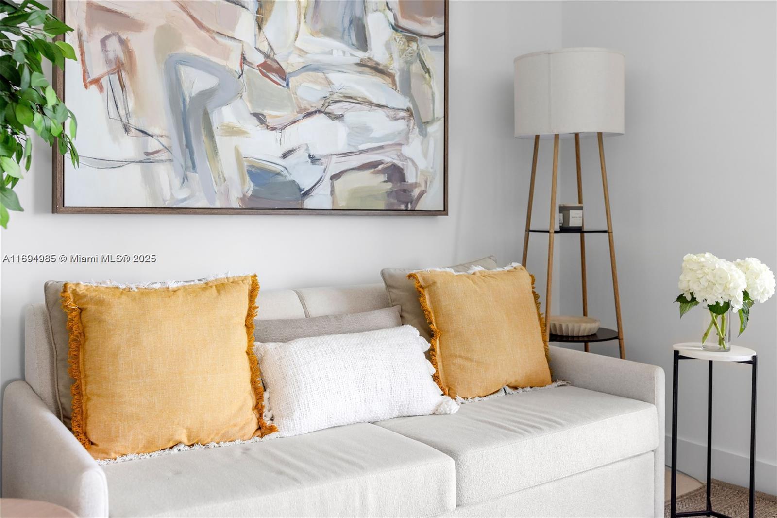 A beige sofa with yellow pillows sits beneath an abstract painting next to a floor lamp — 159 NE 6TH ST # 2916, Miami FL 33132, MIAMI, FL