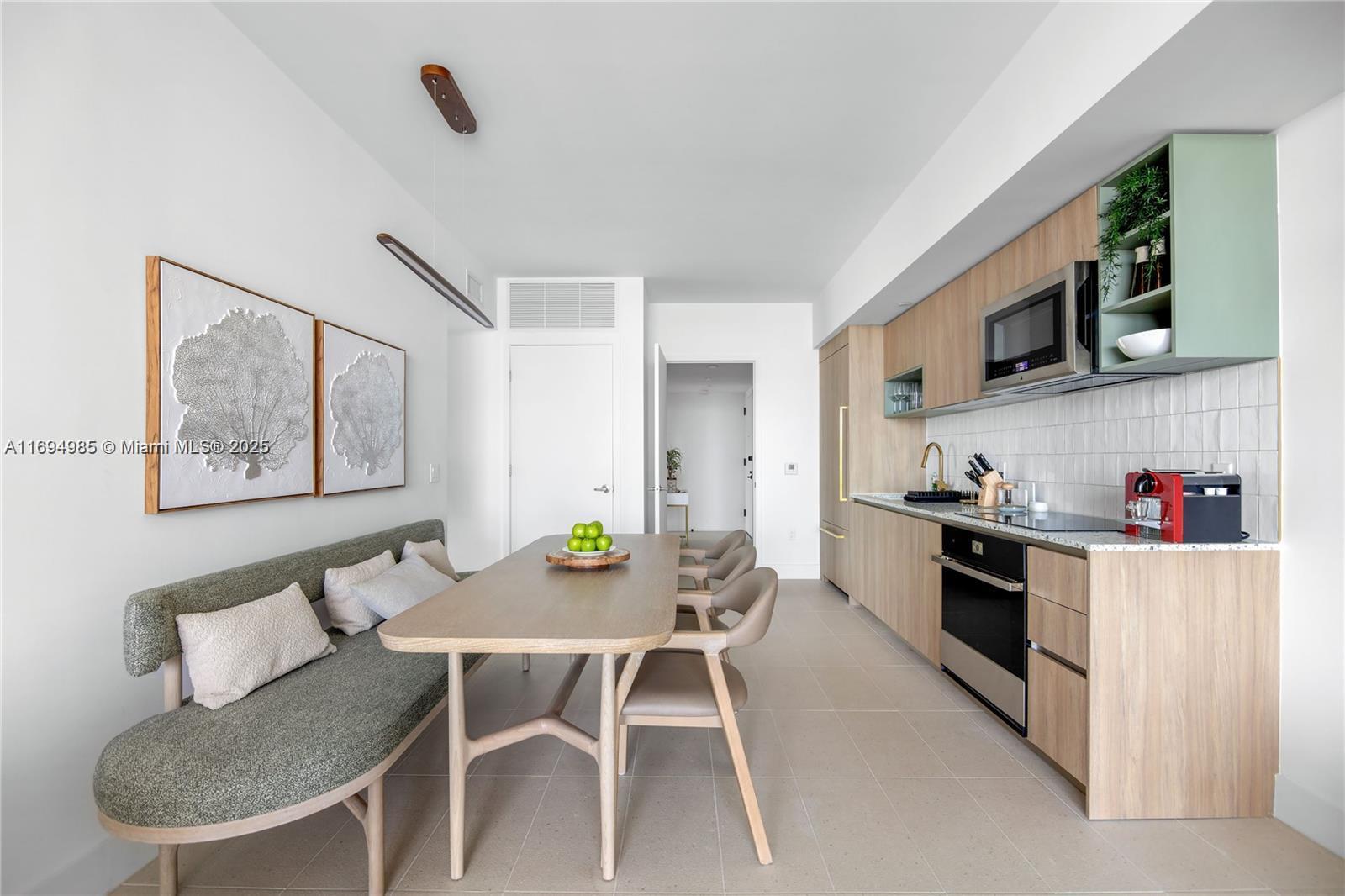 A modern kitchen and dining area features light wood cabinetry, a green banquette, and tile flooring — 159 NE 6TH ST # 2916, Miami FL 33132, MIAMI, FL
