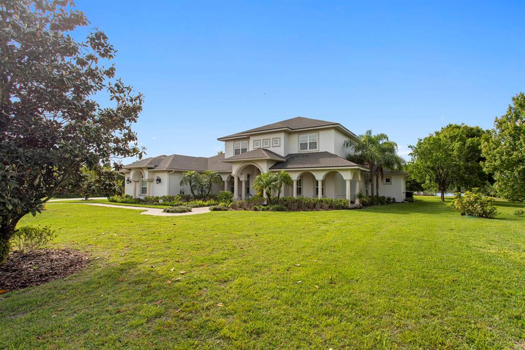 A two-story house with a beige exterior, arched entryway, and a large grassy lawn — 17253 BREEDERS CUP DRIVE, ODESSA, FL