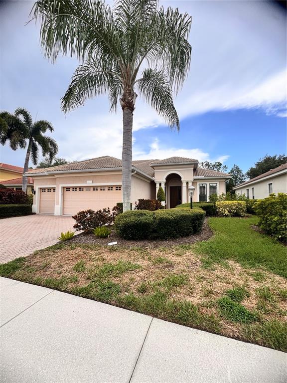 A beige single-story house with a three-car garage and a paved driveway — 13860 SIENA LOOP, BRADENTON, FL