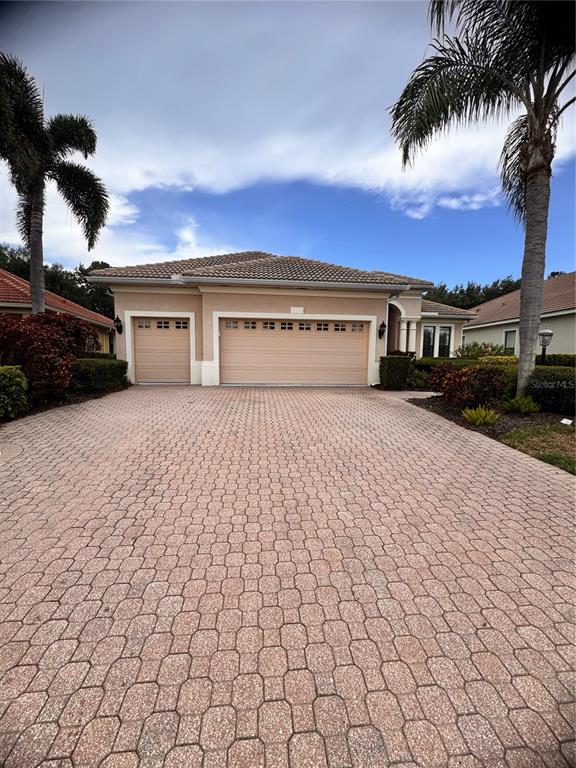 A tan single-story house with a three-car garage and a paved driveway — 13860 SIENA LOOP, BRADENTON, FL