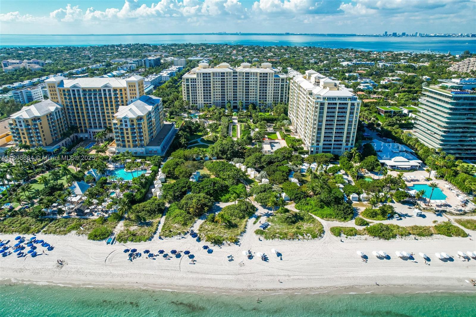 An aerial view shows several large residential buildings surrounded by lush greenery near a beach — 445 Grand Bay Dr # 1001, Key Biscayne FL 33149, KEY BISCAYNE, FL