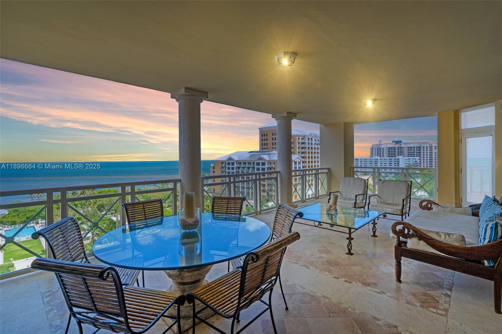 A spacious covered balcony features a glass dining table, seating area, and ocean views — 445 Grand Bay Dr # 1001, Key Biscayne FL 33149, KEY BISCAYNE, FL