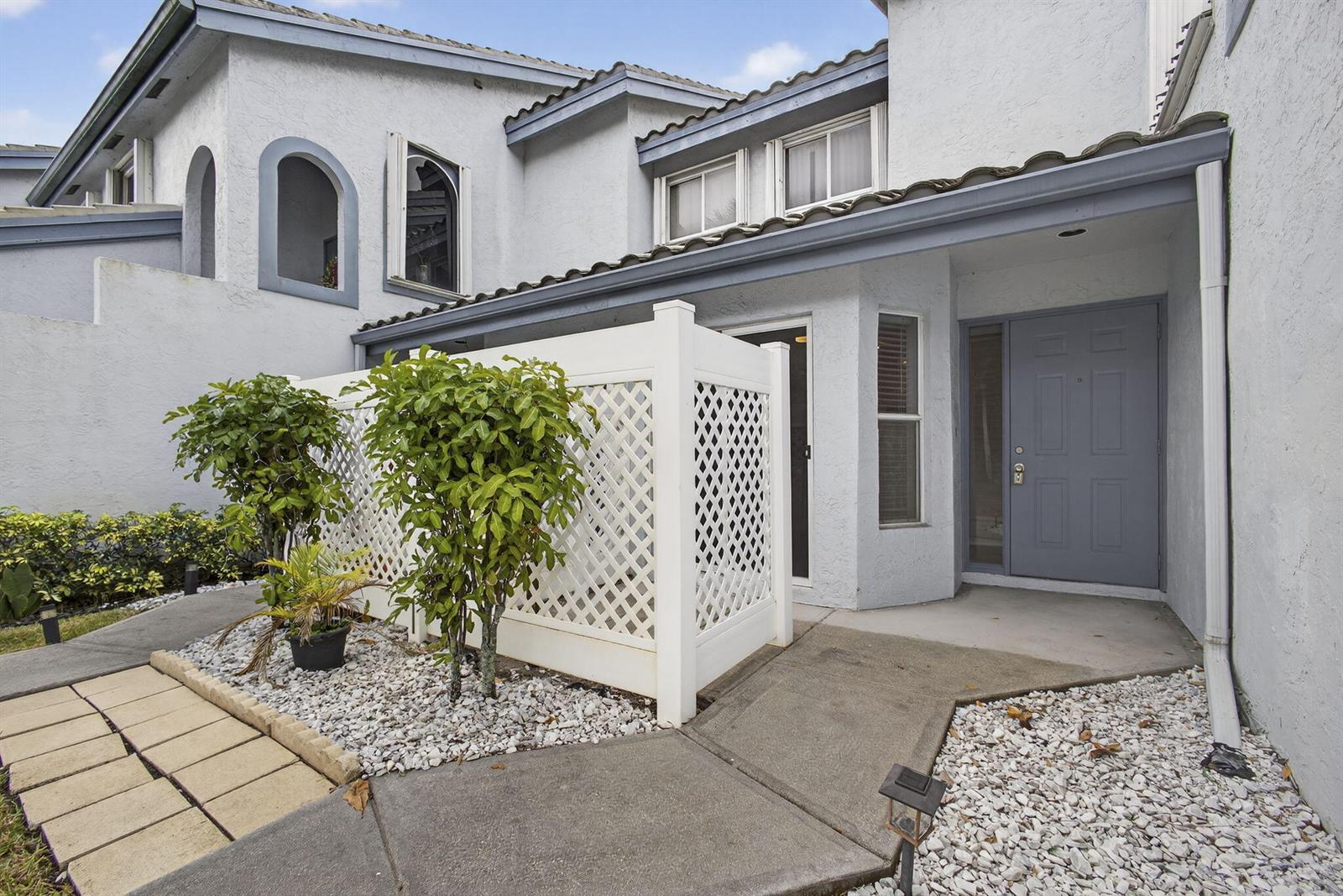 The exterior of a two-story house features a gray front door, white lattice fencing, and a concrete walkway — 9746 Nickels Boulevard # 103, Boynton Beach FL 33436, BOYNTON BEACH, FL