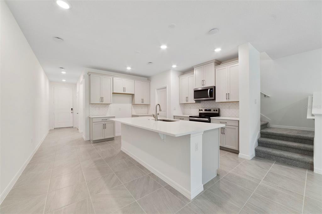 A modern kitchen features light gray cabinets, a white quartz island, and tile flooring — 1657 GREENLEAF WOODS COVE, OVIEDO, FL