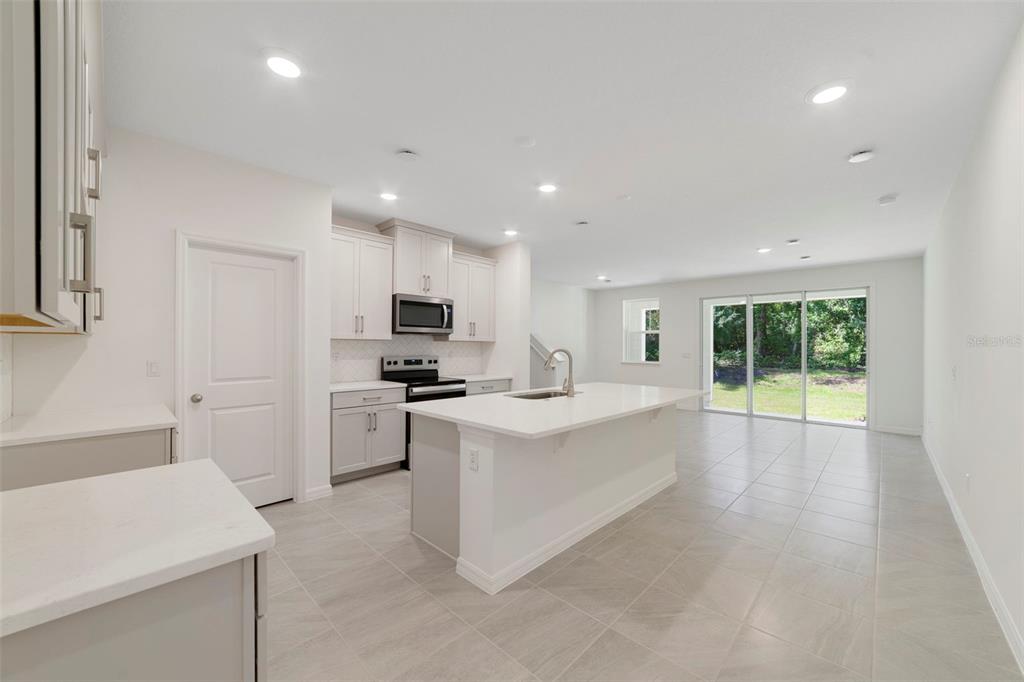 A modern kitchen features white cabinetry, a central island, and tile flooring with sliding doors — 1657 GREENLEAF WOODS COVE, OVIEDO, FL