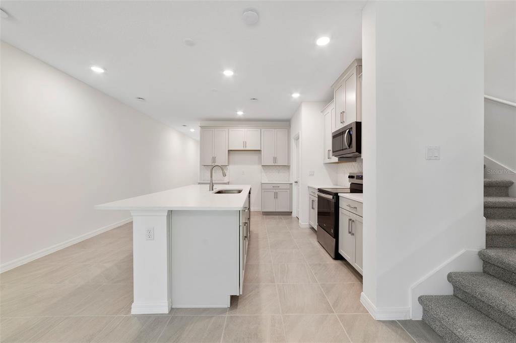 A modern kitchen features light gray cabinets, white countertops, an island, and tile flooring — 1657 GREENLEAF WOODS COVE, OVIEDO, FL
