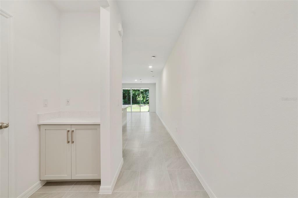 A hallway with light tile flooring leads to a living area with sliding glass doors — 1657 GREENLEAF WOODS COVE, OVIEDO, FL