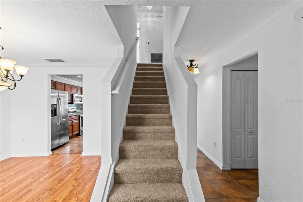 A carpeted staircase leads to an upper landing between a kitchen and a tiled hallway — 8830 ISLA BELLA DRIVE, ORLANDO, FL