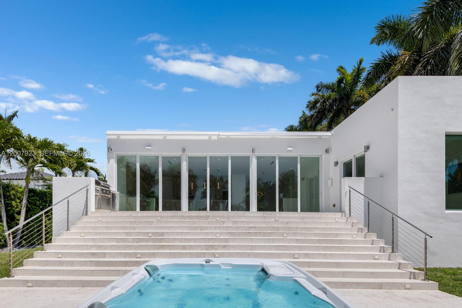 A white modern house features a large staircase leading to a pool and patio area — 1090 NE 84th St, Miami FL 33138, MIAMI, FL