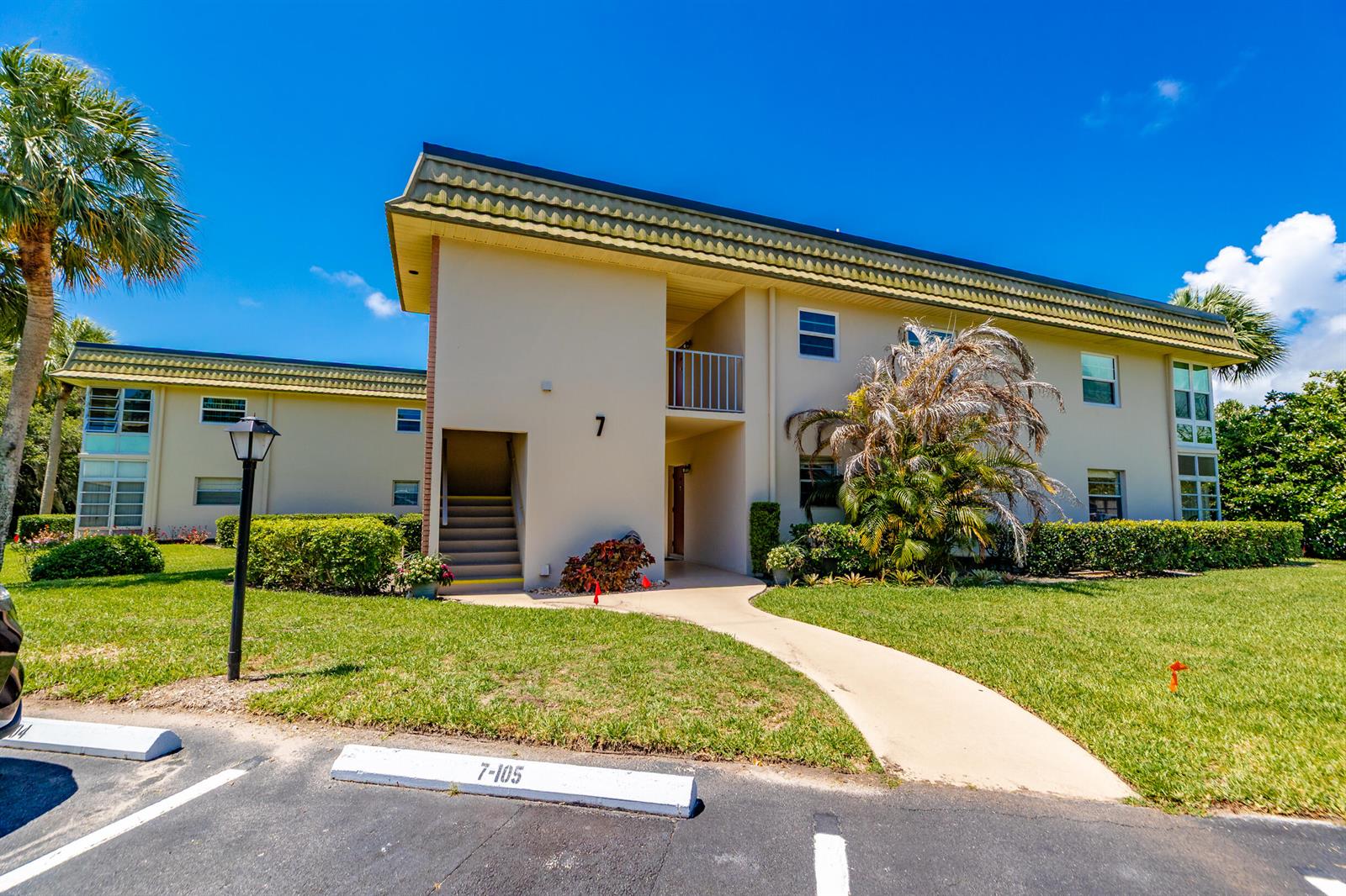 A two-story apartment building features a tan exterior, a green roof, and a concrete walkway — VERO BEACH, FL