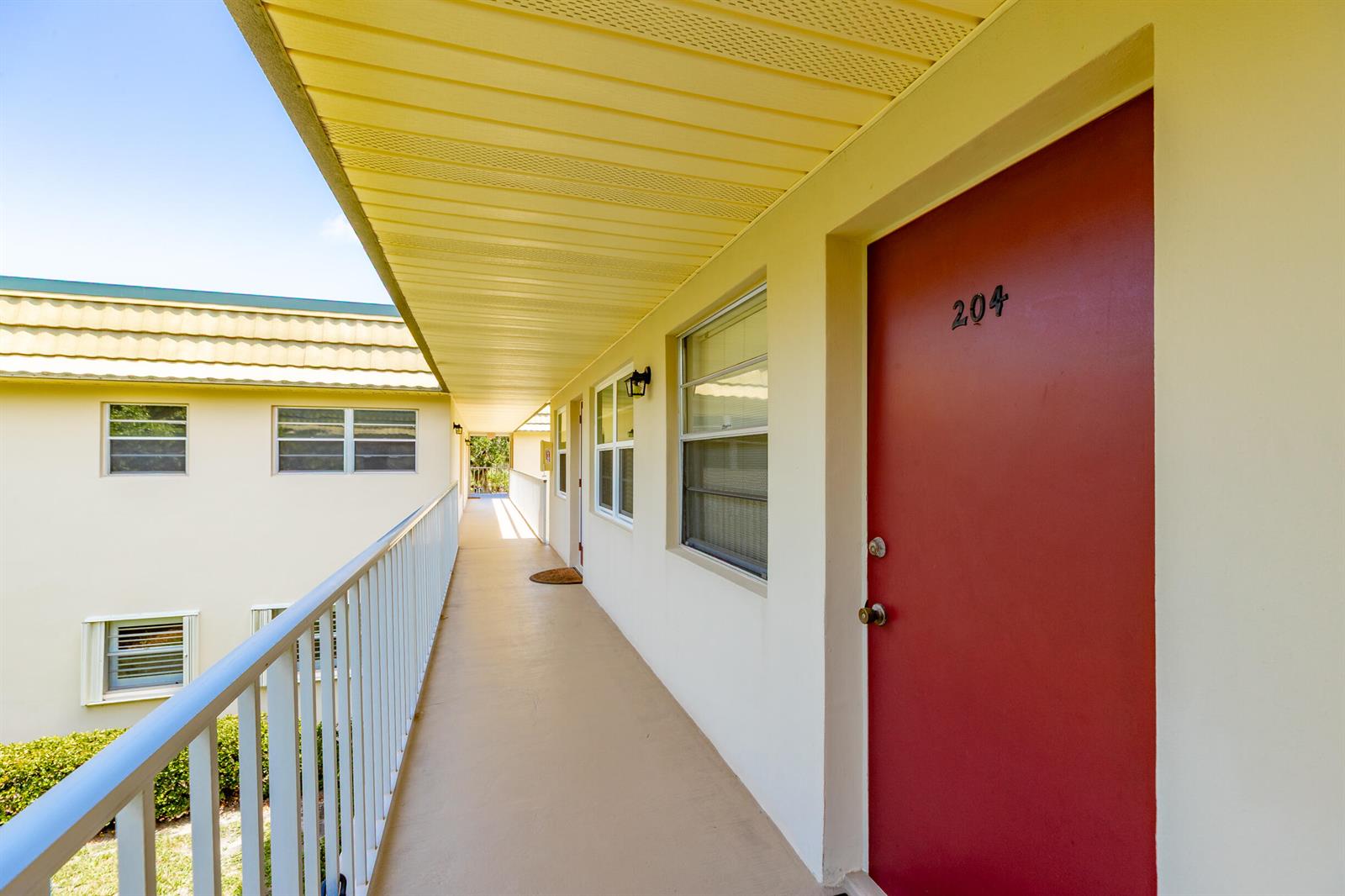 An exterior walkway leads to a red apartment door numbered 204 on a building — VERO BEACH, FL