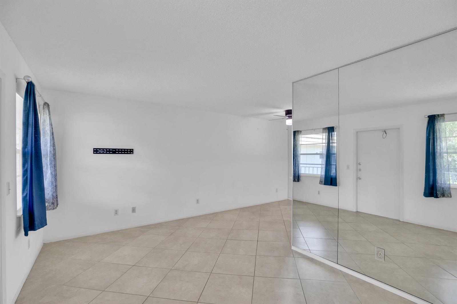 An empty room with white walls, tile flooring, blue curtains, and a large mirrored wall — VERO BEACH, FL