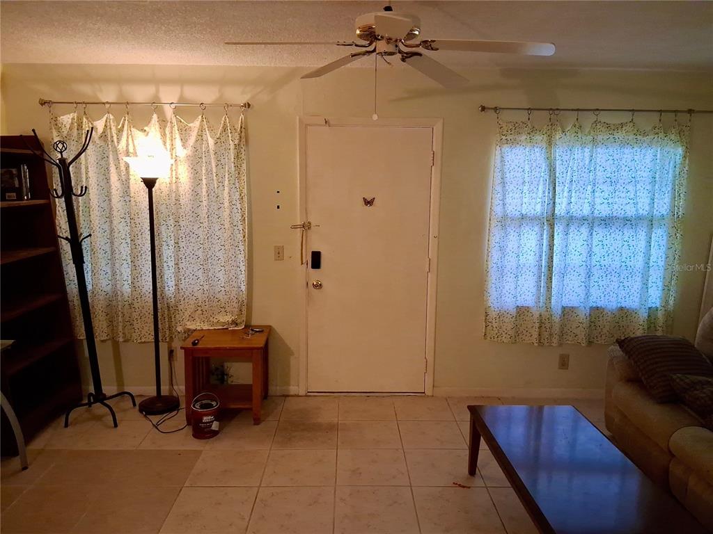 A living room features tile flooring, a ceiling fan, a front door, and window curtains — 1250 S PINELLAS AVENUE UNIT 511, TARPON SPRINGS, FL