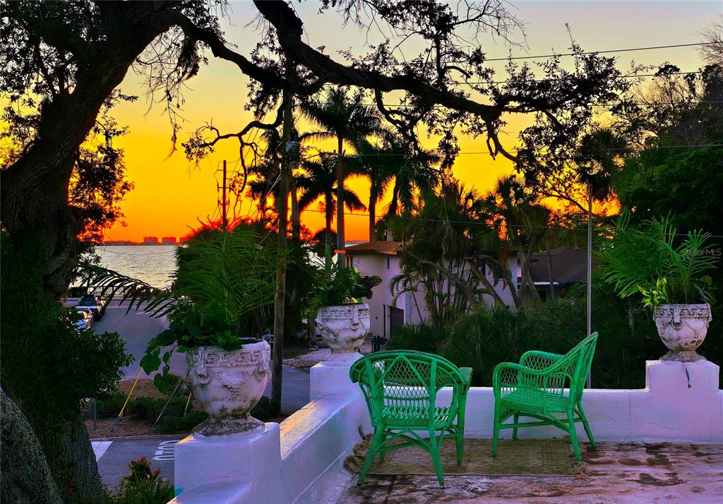A terrace with green wicker chairs and potted plants overlooks a sunset over the water — 2830 BAY SHORE CIRCLE, SARASOTA, FL