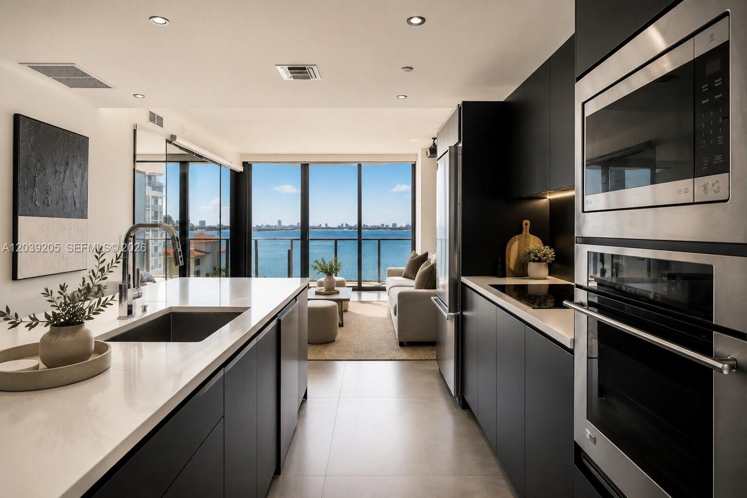 A modern kitchen with dark cabinetry and a white island overlooks a balcony and water — 460 NE 28th St # 805, Miami FL 33137, MIAMI, FL
