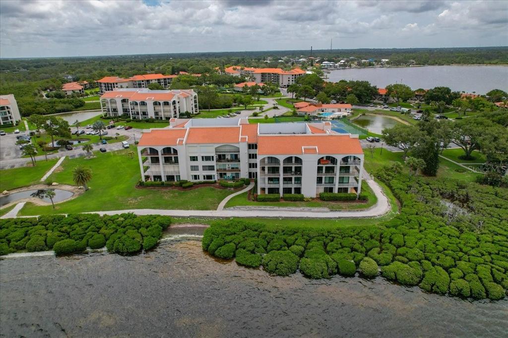 An aerial view shows a multi-story apartment building with a red roof near water — 401 MARINER DRIVE UNIT 401, TARPON SPRINGS, FL